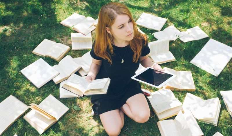 A person sitting on grass with both an e-reader and physical books, representing the choice between modern agile testing and traditional testing approaches