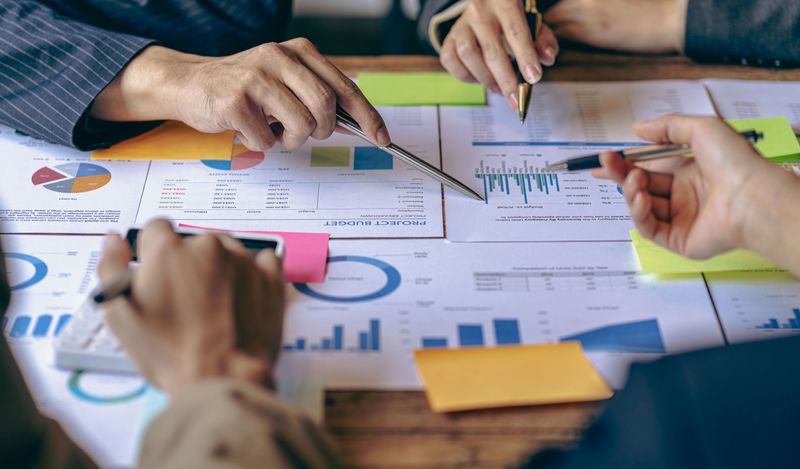 image focuses on printouts of reports with hands in the frame using pens to point at information.