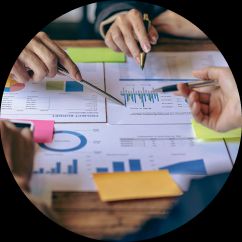image focuses on printouts of reports with hands in the frame using pens to point at information.
